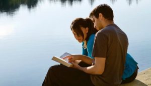 Pár sedící u jezera a který čte písma
